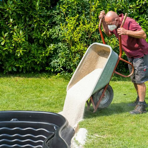 Muž rozhrabáva piesok na trávniku pomocou hrablí