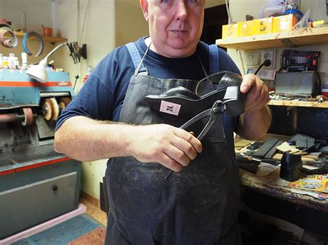 Fotografia obuvníka pri práci, ktorý používa klince na pripevnenie podrážky k topánke.