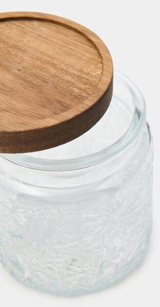 Detailná fotografia sklenenej fľaštičky s dreveným viečkom a bavlnenou šnúrkou ukazujúca umiestnenie tesnenia.