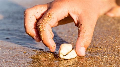 Detailný záber na tvorivý proces pieskovania, kde detská ruka sype farebný piesok na lepkavý podklad šablóny.